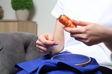 Woman with spool of thread embroidering on cloth at home, closeup