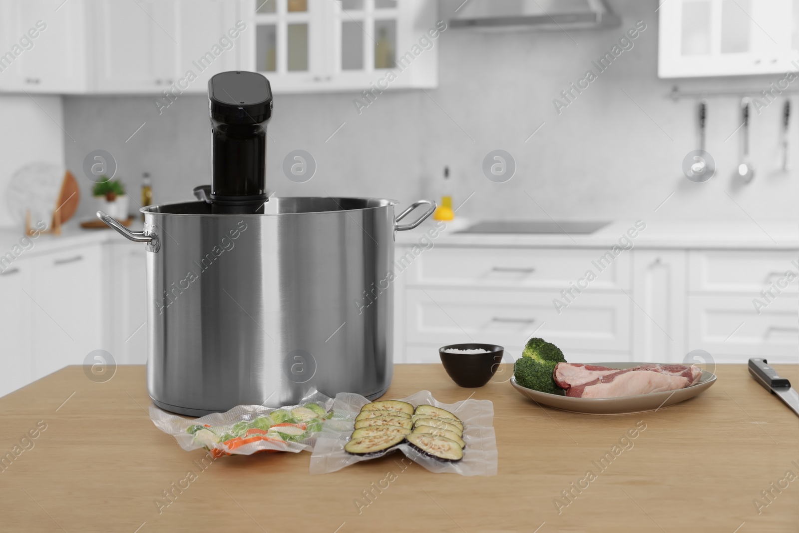 Photo of Pot with sous vide cooker, vacuum packed vegetables and ingredients on table in kitchen. Thermal immersion circulator