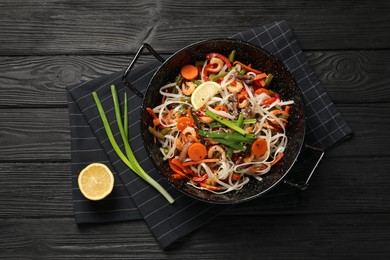 Shrimp stir fry with noodles and vegetables in wok on black wooden table, top view