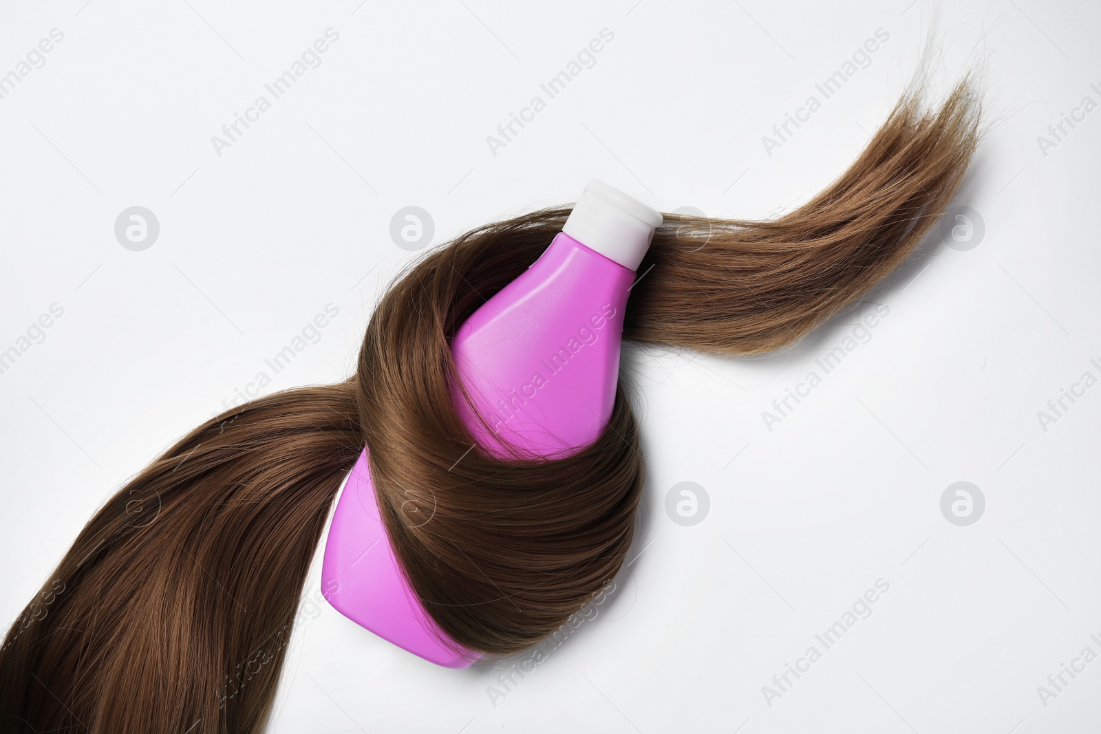 Photo of Shampoo bottle wrapped in lock of hair on white background, top view. Natural cosmetic products