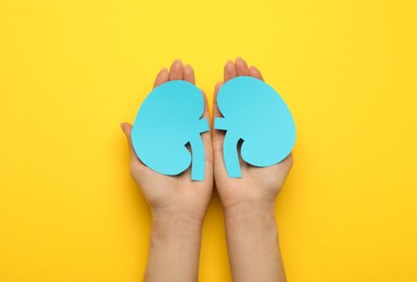 Photo of Woman holding paper cutout of kidneys on yellow background, top view