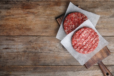 Photo of Raw meat cutlets for burger on wooden table, top view. Space for text