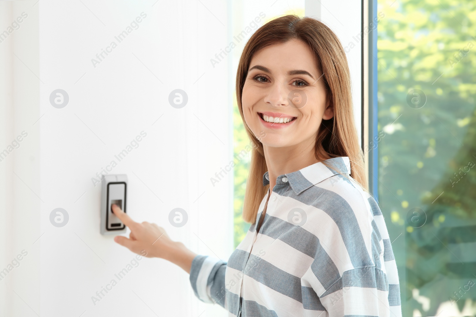 Photo of Young woman pressing fingerprint scanner on alarm system indoors