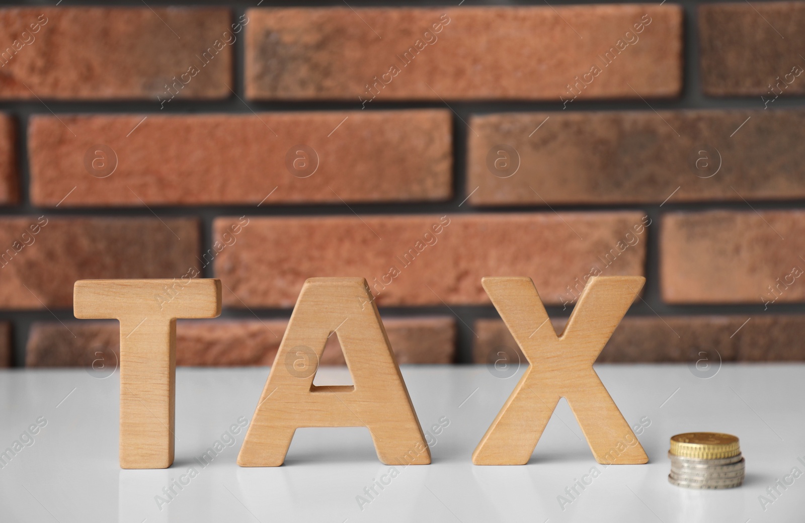 Photo of Word TAX made of letters and coins on table against brick wall