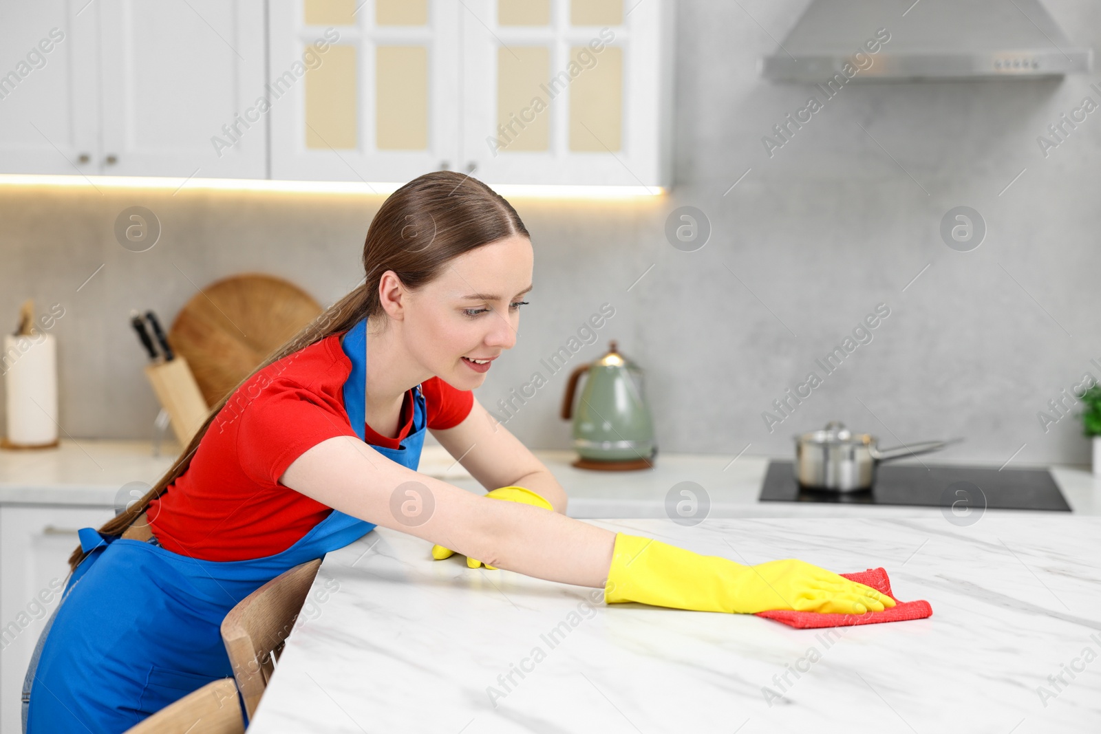 Photo of Woman cleaning white marble table with rag in kitchen, space for text