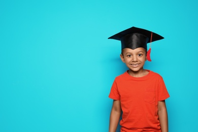 Little African-American school child with graduate cap on color background