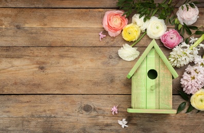 Flat lay composition with bird house and flowers on wooden background. Space for text