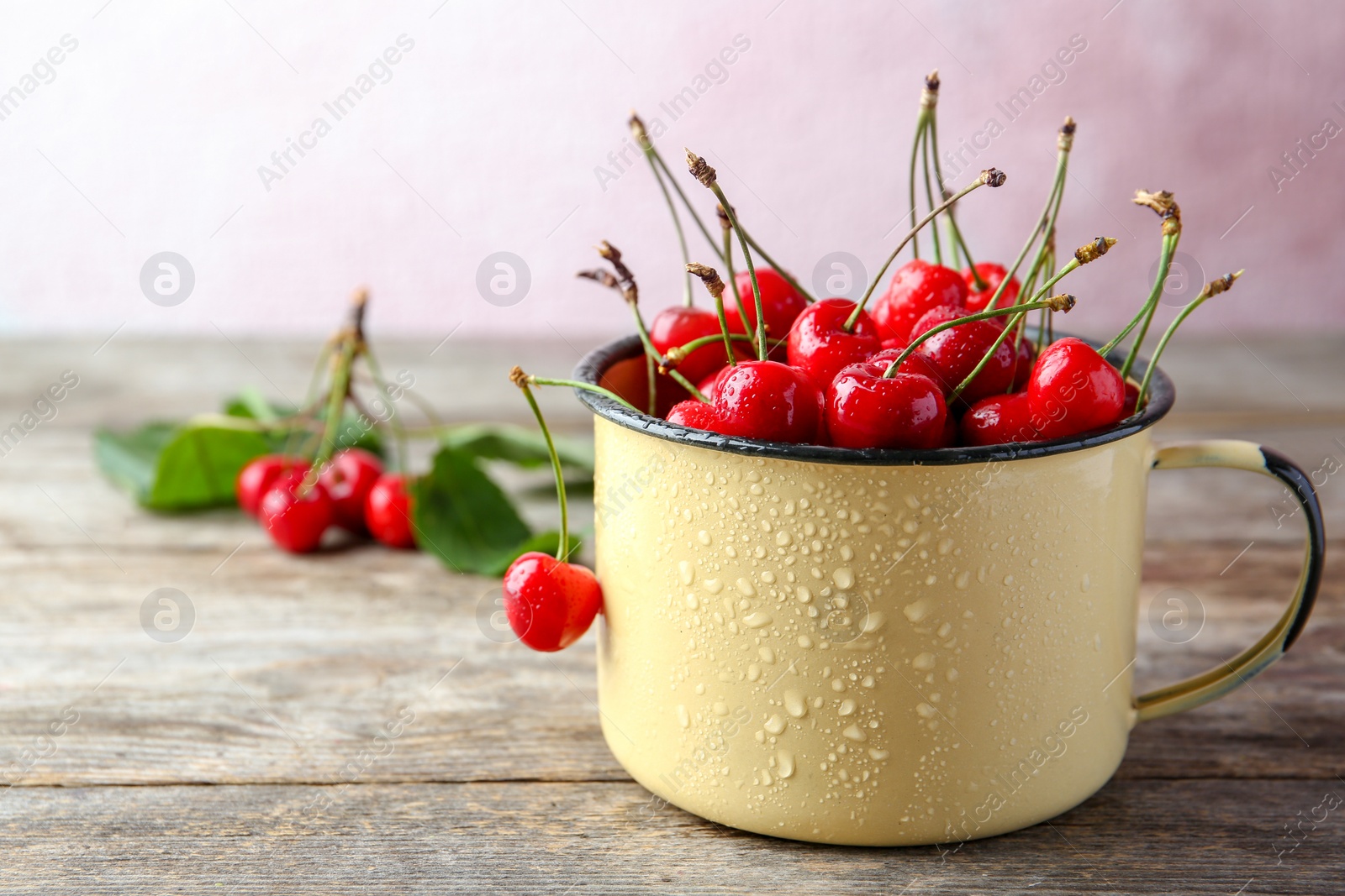 Photo of Metal mug with ripe red cherries on wooden table