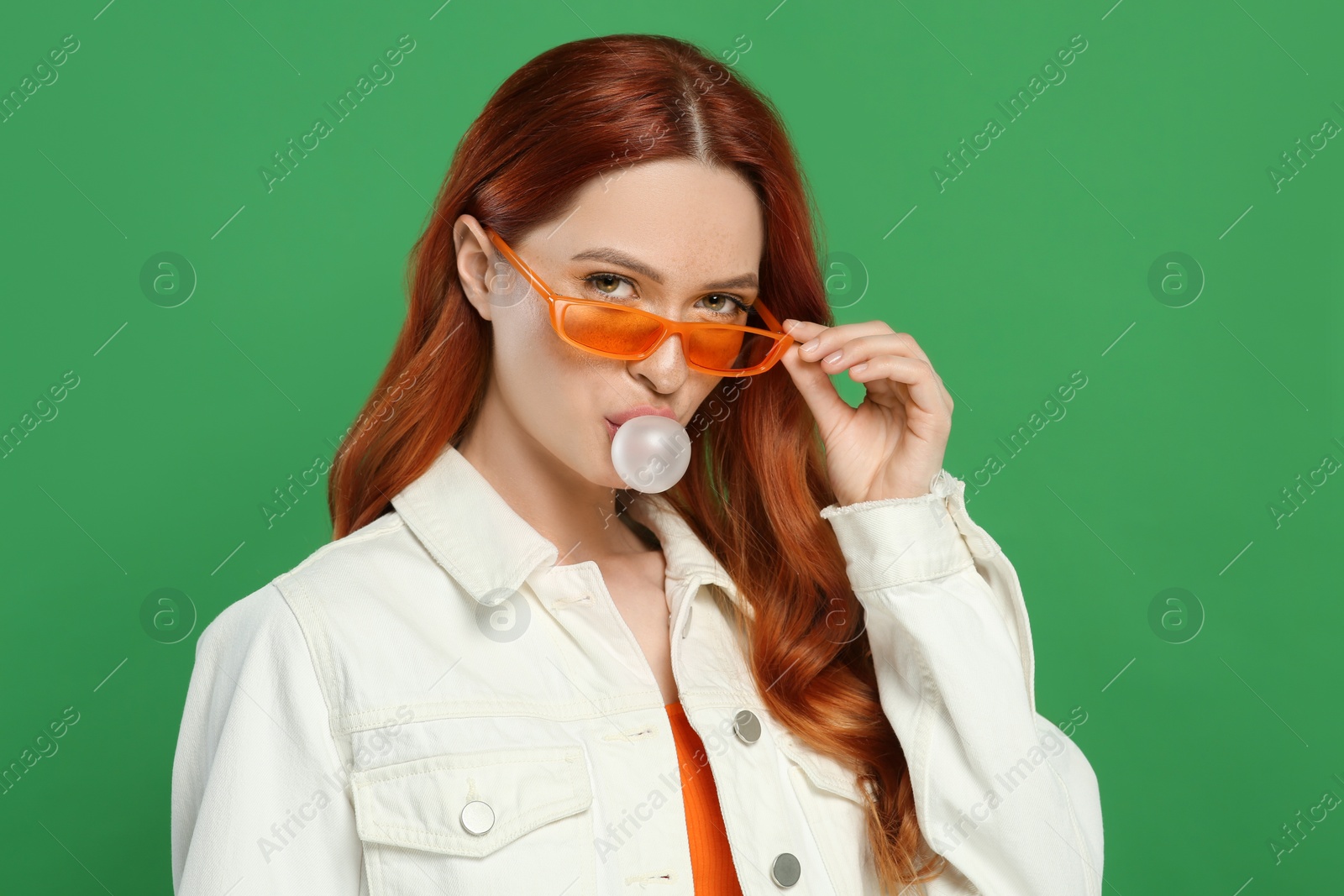 Photo of Portrait of beautiful woman in sunglasses blowing bubble gum on green background