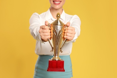 Photo of Young businesswoman with gold trophy cup on yellow background, closeup