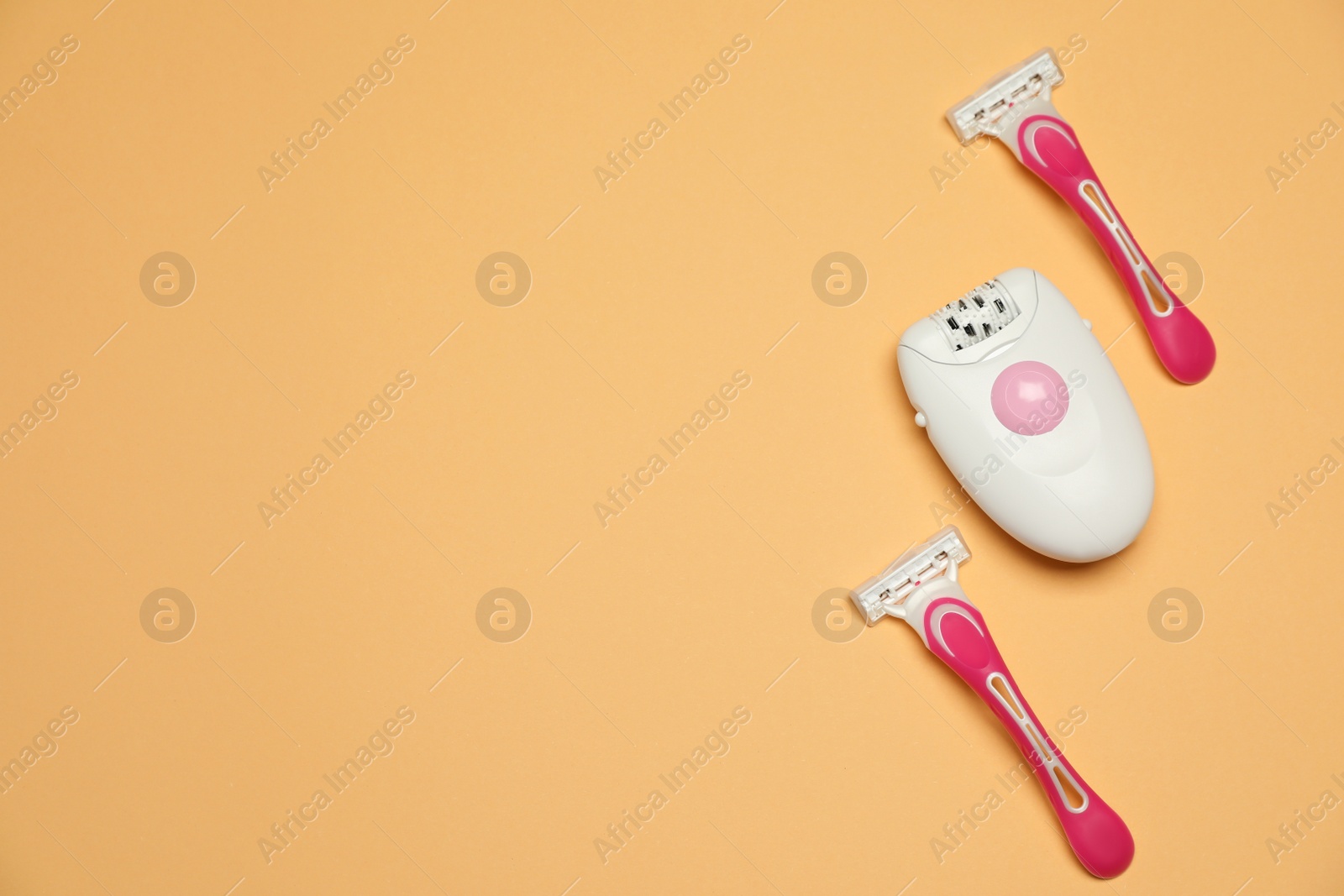 Photo of Modern epilator and razors on orange background, flat lay. Space for text