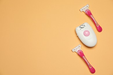 Photo of Modern epilator and razors on orange background, flat lay. Space for text