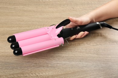 Photo of Woman holding modern triple curling iron on wooden background, closeup