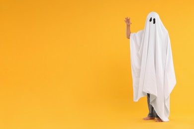 Photo of Woman in white ghost costume on yellow background, space for text. Halloween celebration