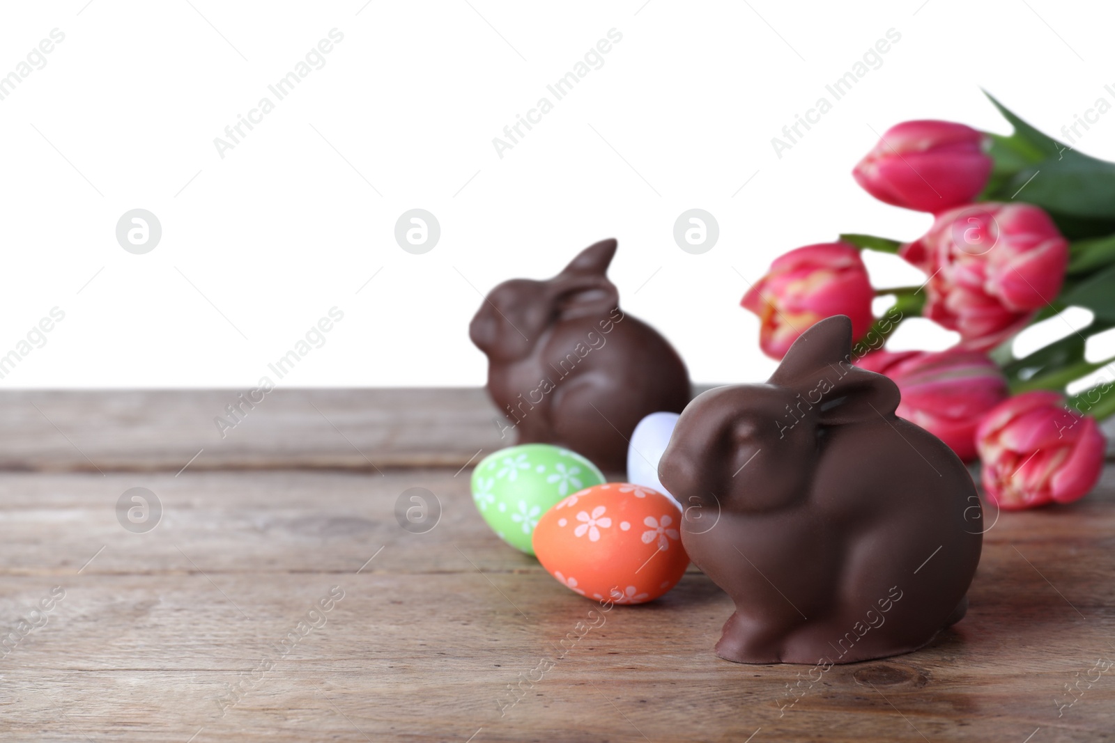 Photo of Chocolate Easter bunny, eggs and tulips on wooden table against white background. Space for text