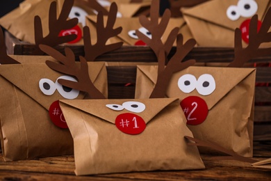 Photo of Gifts in envelopes with deer faces on wooden table, closeup. Christmas advent calendar