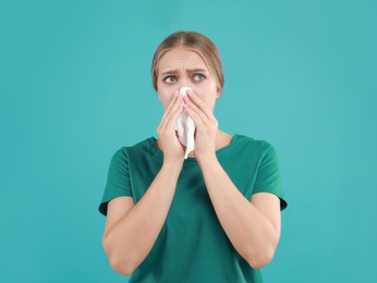 Young woman suffering from allergy on turquoise background