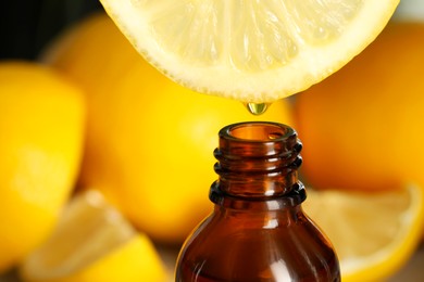 Photo of Dripping essential oil from lemon into bottle on blurred background, closeup