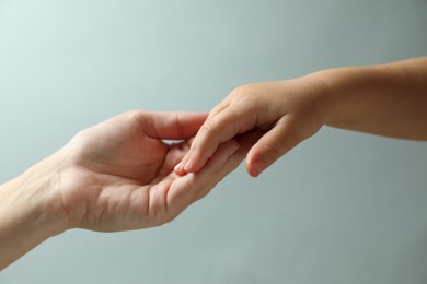 Photo of Mother and child holding hands on light blue background, closeup