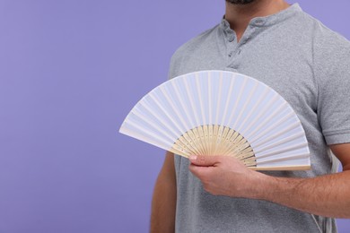 Man holding hand fan on purple background, closeup. Space for text