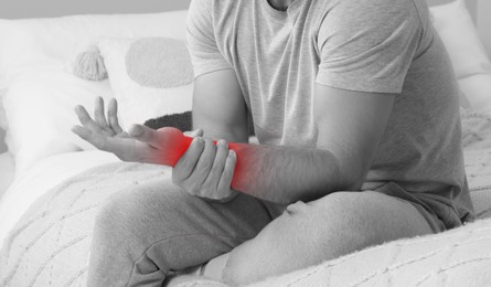 Man suffering from pain in hand on bed, closeup. Black and white effect. Banner design