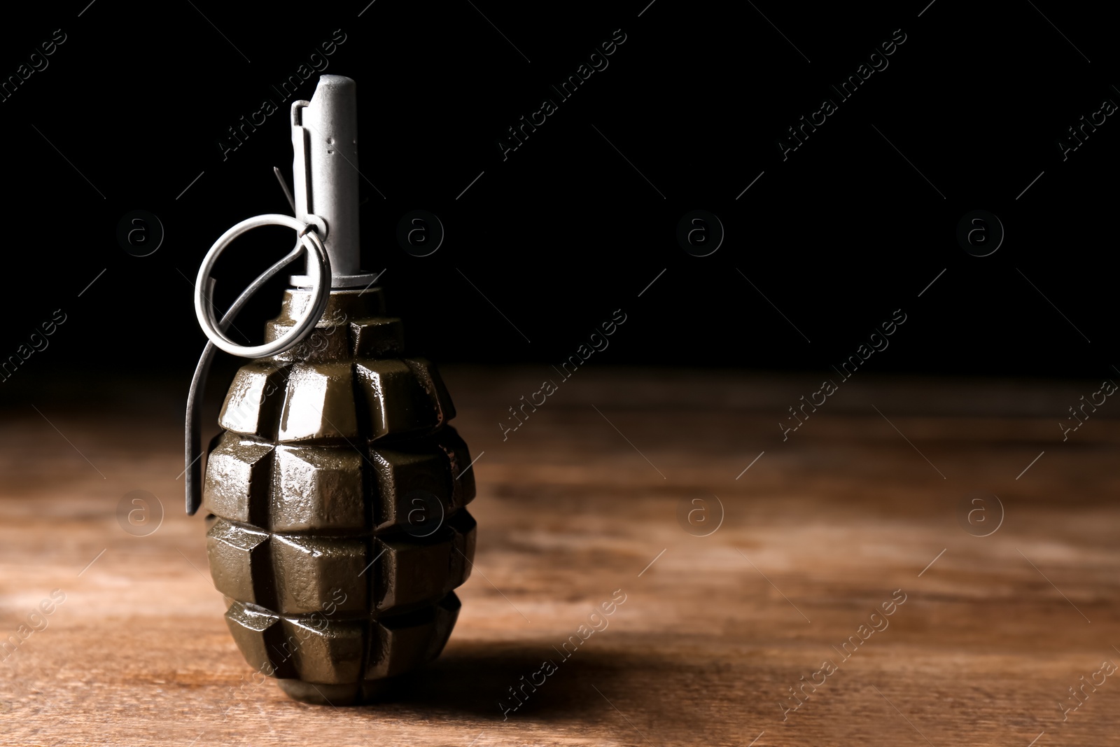 Photo of Hand grenade on wooden table against black background. Space for text