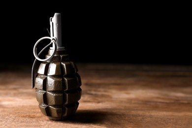 Photo of Hand grenade on wooden table against black background. Space for text