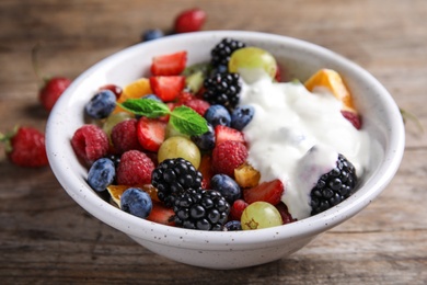 Photo of Fresh tasty fruit salad with yogurt on wooden table, closeup