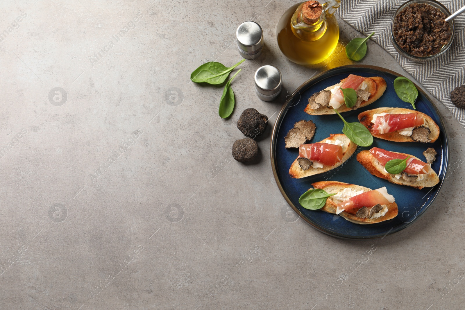 Photo of Delicious bruschettas with cheese, prosciutto and slices of black truffle on grey table, flat lay. Space for text