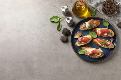 Delicious bruschettas with cheese, prosciutto and slices of black truffle on grey table, flat lay. Space for text