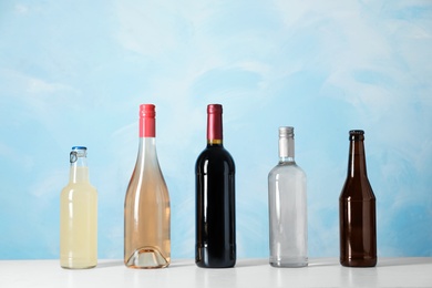 Bottles with different alcoholic drinks on table against color background