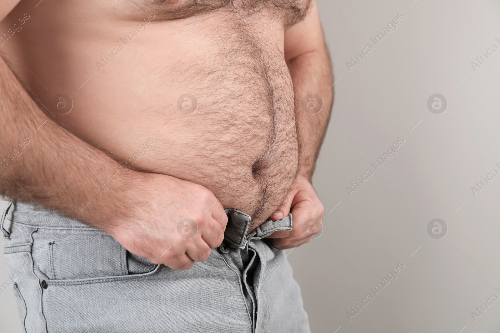 Photo of Overweight man trying to button jeans on color background, closeup. Space for text