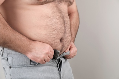 Photo of Overweight man trying to button jeans on color background, closeup. Space for text