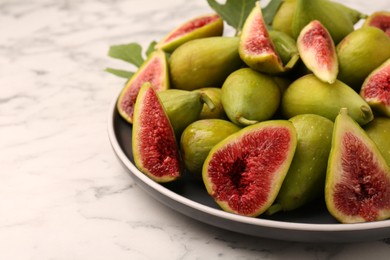 Cut and whole green figs on white marble table, closeup