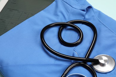 Photo of Stethoscope in shape of heart on light blue medical uniform, closeup