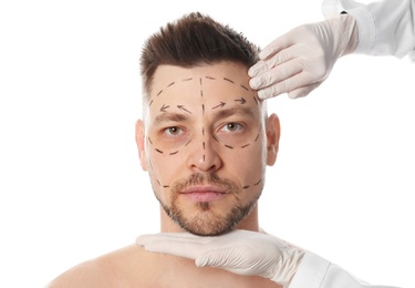 Doctor examining man's face before plastic surgery operation on white background