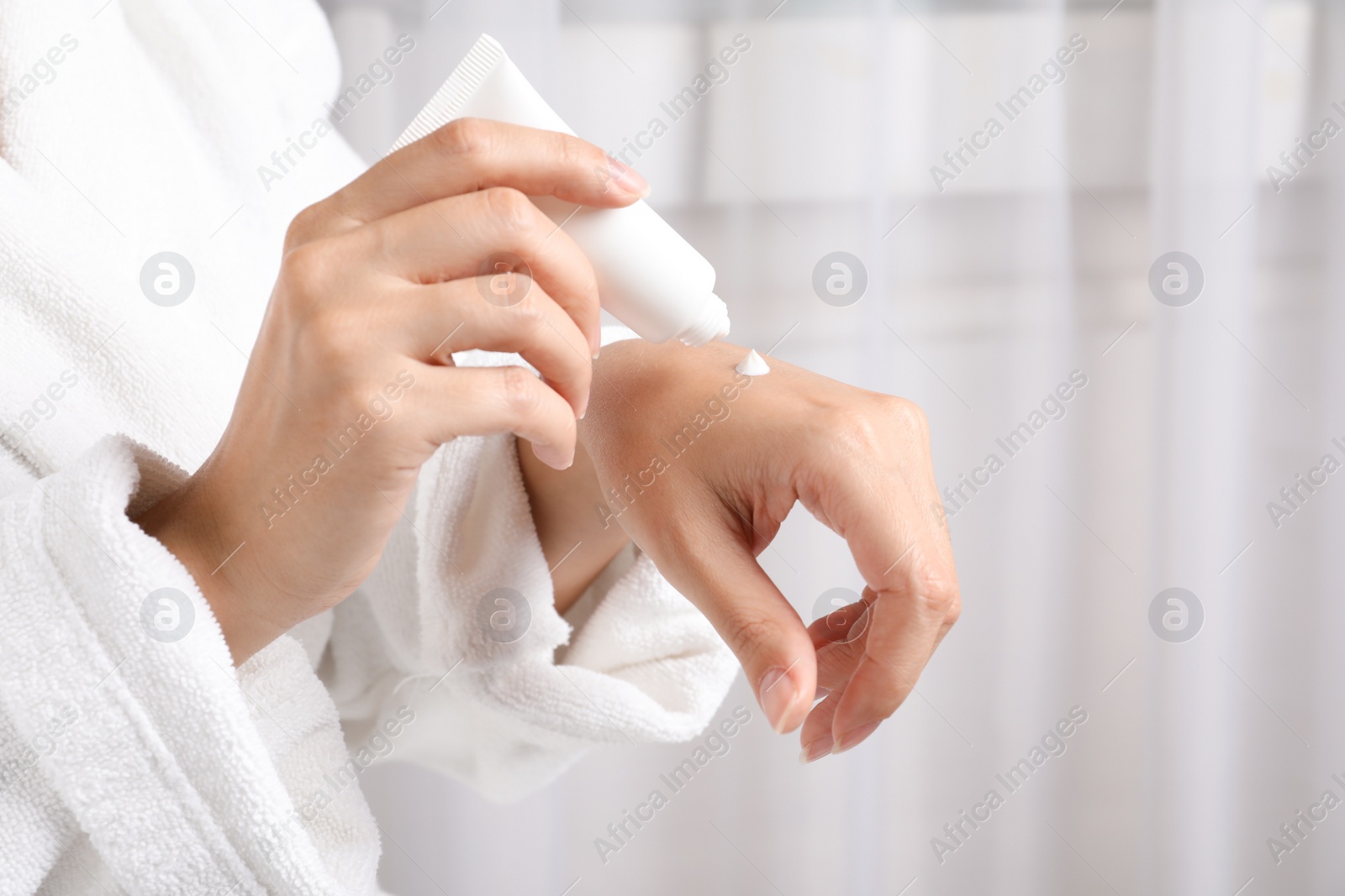 Photo of Woman in bathrobe applying moisturizing hand cream, closeup. Winter skin care cosmetic