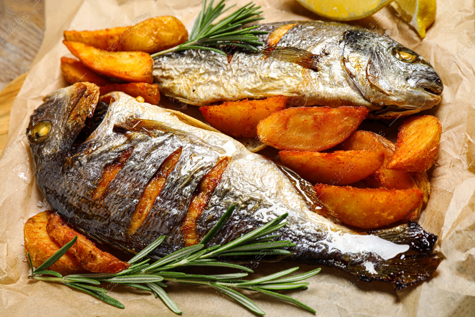 Photo of Delicious roasted fish and potatoes on parchment paper, closeup