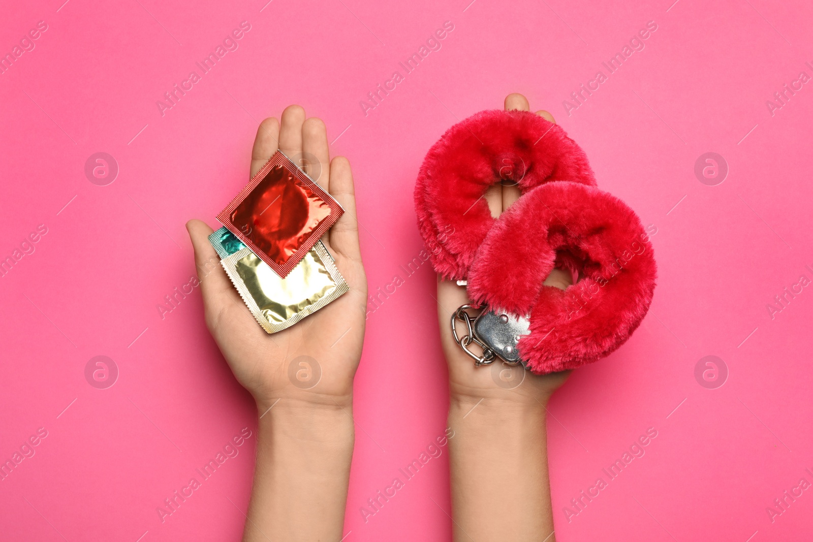 Photo of Woman with furry handcuffs and condoms on pink background, top view. Sex game