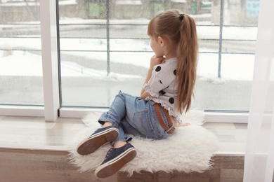 Photo of Lonely little girl sitting near window indoors. Autism concept