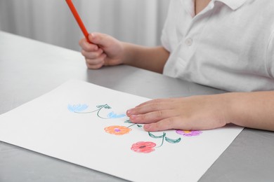 Photo of Little boy drawing flowers with pencil at grey table indoors, closeup. Child`s art