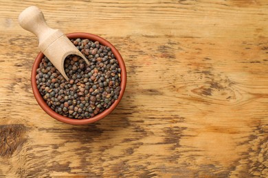 Raw lentils and scoop in bowl on wooden table, top view. Space for text