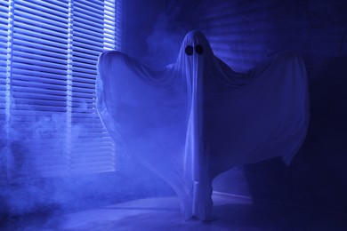 Photo of Creepy ghost. Woman covered with sheet near window in blue light