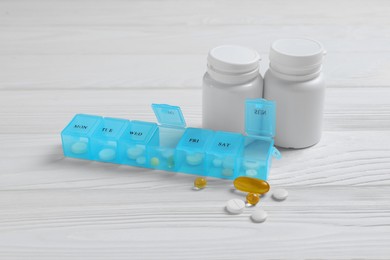 Weekly pill box and containers with medicaments on white wooden table