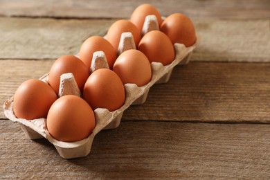 Raw chicken eggs in carton on wooden table, closeup. Space for text