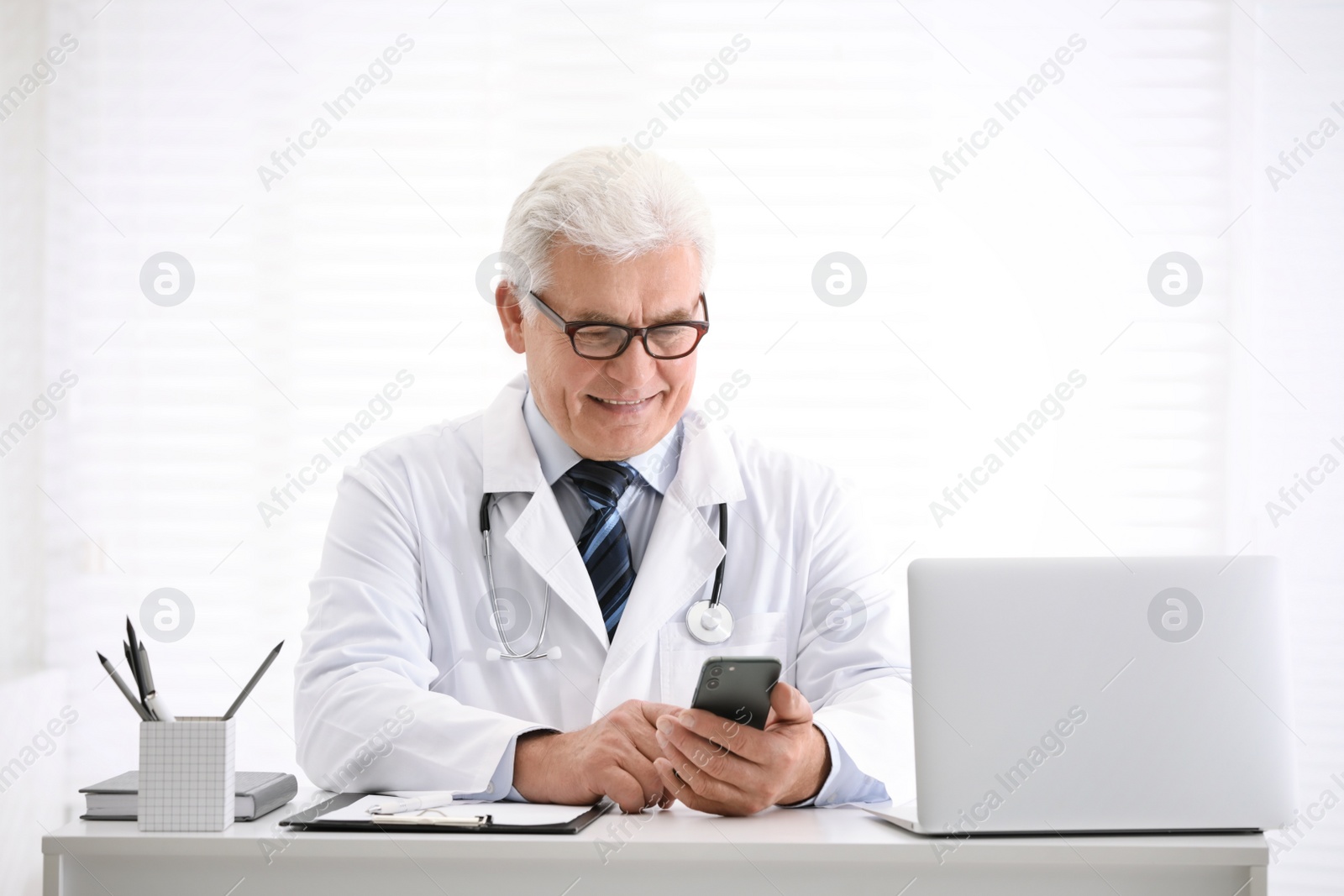 Photo of Senior doctor with smartphone at table in office