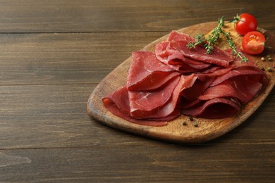 Photo of Tasty bresaola, peppercorns, tomatoes and thyme on wooden table. Space for text