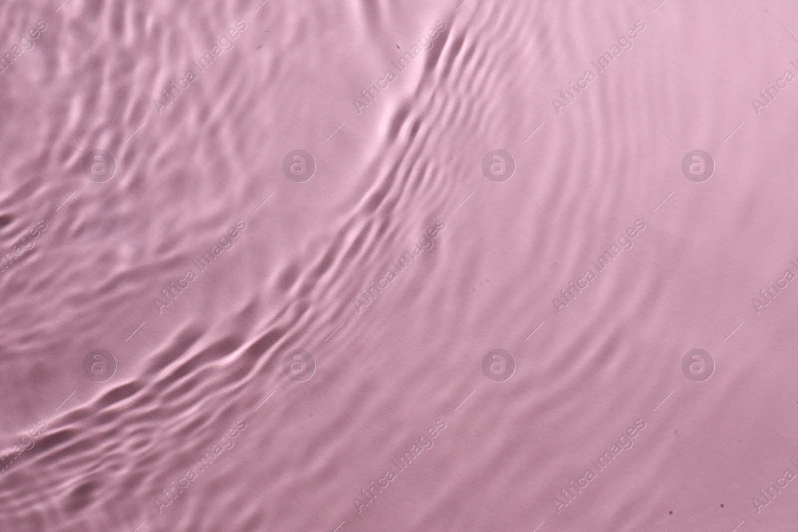 Photo of Rippled surface of clear water on pink background, top view