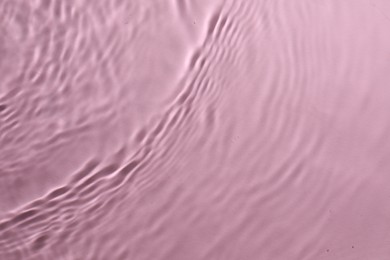 Rippled surface of clear water on pink background, top view