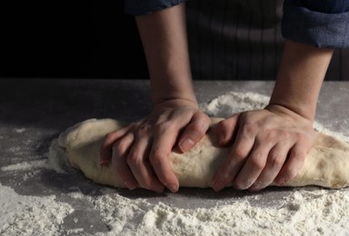 Making bread. Woman kneading dough at table on dark background, closeup